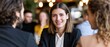 © gunzexx png and bg - A confident young woman smiles while engaging with two colleagues in a modern, vibrant cafe setting, showcasing professionalism and social interaction among peers.