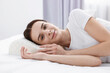 © New Africa - Woman lying on bed with orthopedic pillow at home