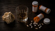 © Teeradej - Lifestyle risk factors for sexual dysfunction. Flat lay of an empty whiskey glass, scattered prescription pill bottles, and a crumpled stress ball on a dark wooden surface.