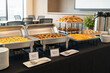 © AiHRG Design - There is a buffet table with trays of food in a meeting room. The food options include vegetarian dishes, gluten-free items, pastries, and fruit slices. The setting is for a group of people.