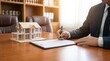 © areeba - Real estate agent signing a house purchase contract with a model house on desk