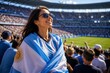 © crispy - Happy woman supporter wrapped in Argentina flag at soccer stadium. Fan watching professional football match during championship. Sport emotion, stadium atmosphere and tournament energy