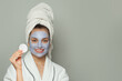 © artmim - Woman applies face mask at home during the evening while smiling and holding a cotton pad in her hand