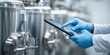 © Evgenii - Worker inspecting production line tanker in factory using computer. Gloved hands with a digital tablet on steel tanks background. Brewery fermentation Monitoring. Advanced tools. Food industry banner.