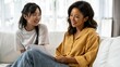 © Premium_art - Two women joyfully sharing ideas while sitting on a couch in a bright living room.