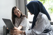 © Odua Images - Two women sitting together on a sofa review a laptop screen while smiling and talking in a softly lit room near a window