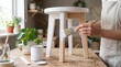 © Radiant Art - Person painting a wooden stool with white paint at home workbench