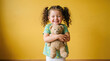© Pixel Commerce Co - Joyful toddler hugging teddy bear against bright yellow wall