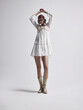 © Cumhur - Boho Chic Fashion Editorial: White Tiered Mini Dress and Gold Western Boots with Arms Raised Pose