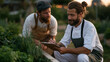 © forenna - Seed to table restaurant garden tour at sunrise, a head chef crouching beside a raised herb bed with a clipboard and a farmer, planning the evening menu based on what is ready to