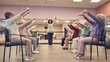 © swillklitch - Group of elderly people doing chair fitness exercise with bells in community center class