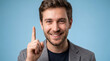 ©  Kibria Islam - Young man in a gray blazer points his index finger upward to indicate a bright idea or an important point against a blue background.
