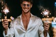 © whitestorm - Smiling young man with sunglasses holding sparklers at night with bokeh lights in background