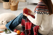 © Pixel-Shot - Woman holding mason jar of hot mulled wine, fruits and warm plaid sitting on floor at home