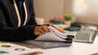 © NanSan - Businesswoman reviewing a stack of documents at an office desk with charts, binder clips and laptop, showing paperwork, analysis and everyday administrative work.
