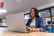 © wavebreak3 - Adult woman with smartwatch working on silver laptop at light-wood table in open office, copy space