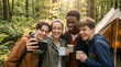 © Illustratorstock - Four happy teenagers taking a group selfie while camping in the woods. Smiling friends enjoying a fun outdoor summer hangout with cups and a tent. Youth lifestyle concept.