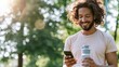 © Bonsales - Young man smiling at smartphone, holding reusable water bottle, enjoying active lifestyle outdoors