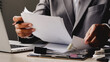 © WARAPHON - Businessman reviews documents near laptop. Focused, serious demeanor suggests decision-making. Desk holds papers, pens, and office supplies. Professional setting implies productivity and strategy