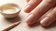 © Yevhen - A close-up of a woman's hand with neatly manicured nails. A small bowl of oil and a wooden stick are placed nearby. The background is soft and neutral.