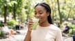 © Olga Ко - Beautiful smiling African American woman drinking an iced matcha latte outdoors in a sunny city park. Healthy summer beverage and wellness concept