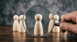 © Md Arif Babu - Magnifying glass focusing on wooden figure, human resources recruitment concept, talent search and candidate selection process