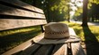 © ABDUL - . Straw hat resting on a wooden park bench, sunny park, peaceful summer atmosphere