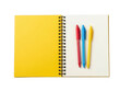 © Skstor - Open spiral bound notebook with yellow cover and three colorful pens on white pages.