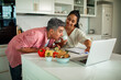 © Marko Geber - Couple preparing vegetables and checking recipes on laptop in modern kitchen