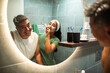 © Marko Geber - Happy couple applying facial mask in home bathroom mirror