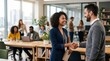 © Irina Kalinina - Smiling professional man and woman shake hands in a modern open space office with colleagues working in the background, successful corporate partnership, diverse business teamwork scene.