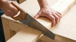 © Kroul - Craftsperson using hand saw to cut wooden plank on workbench