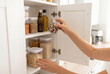 © Meow Creations - Woman selecting a glass jar of dry beans from an organized white kitchen cabinet