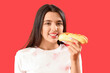 © Pixel-Shot - Pretty young woman with tasty hot dog on red background