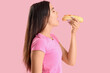 © Pixel-Shot - Pretty young woman eating tasty hot dog on pink background