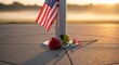 © ZHMPRO - American flag and single red rose at base of flagpole with golden sunrise and foggy background, remembrance concept.