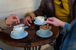 © DusanJelicic - Three friends sitting around a small wooden table, stirring and drinking coffee, sharing moments of relaxation and social interaction at an outdoor cafe