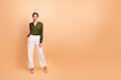 © deagreez - Confident businesswoman model wearing green blouse and white pants in beige studio background