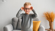 © dinatychynska - Happy child boy wearing eyeglasses at home smiling. Young kid adjusting new spectacles frames. Vision correction optical healthcare concept. Blonde preschooler in grey sweater living room interior.