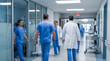 © Celt Studio - Motion blurred medical professionals wearing blue scrubs walking hurriedly down bright hospital corridor responding quickly to incoming critical patient emergency situation