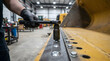© Mahmuda - mechanic using socket wrench on heavy machinery | industrial maintenance and repair workshop | heavy equipment bucket repair with hand tools | professional technician working on construction vehicle