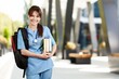 © BillionPhotos.com - Medical student in blue scrubs holding books and backpack on a modern university campus