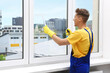 © New Africa - Worker washing window with squeegee and detergent indoors