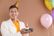 © New Africa - Happy man holding piece of cake with burning candle and colorful balloons on brown background. Space for text