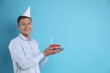 © New Africa - Man holding piece of cake with burning candle on light blue background, space for text