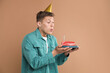 © New Africa - Man blowing candle on piece of delicious cake against pale brown background