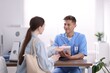 © New Africa - Medical assistant helping patient at desk in clinic