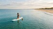 © velikiyzayats - Young woman kneeling on stand up paddle board in calm turquoise ocean water near sandy beach at sunrise for summer vacation travel and active lifestyle concept