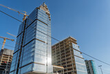 Modern office skyscrapers under construction in Belgrade, Serbia, with glass facades, cranes, exposed concrete floors and blue sky, showing real estate and business development.