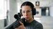 © SITI - Focused female shooter wearing ear muffs and safety glasses aiming sniper rifle at target inside shooting range